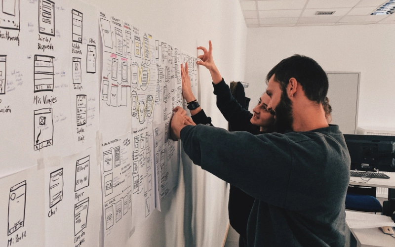 Some people looking at a white board covered in notes.